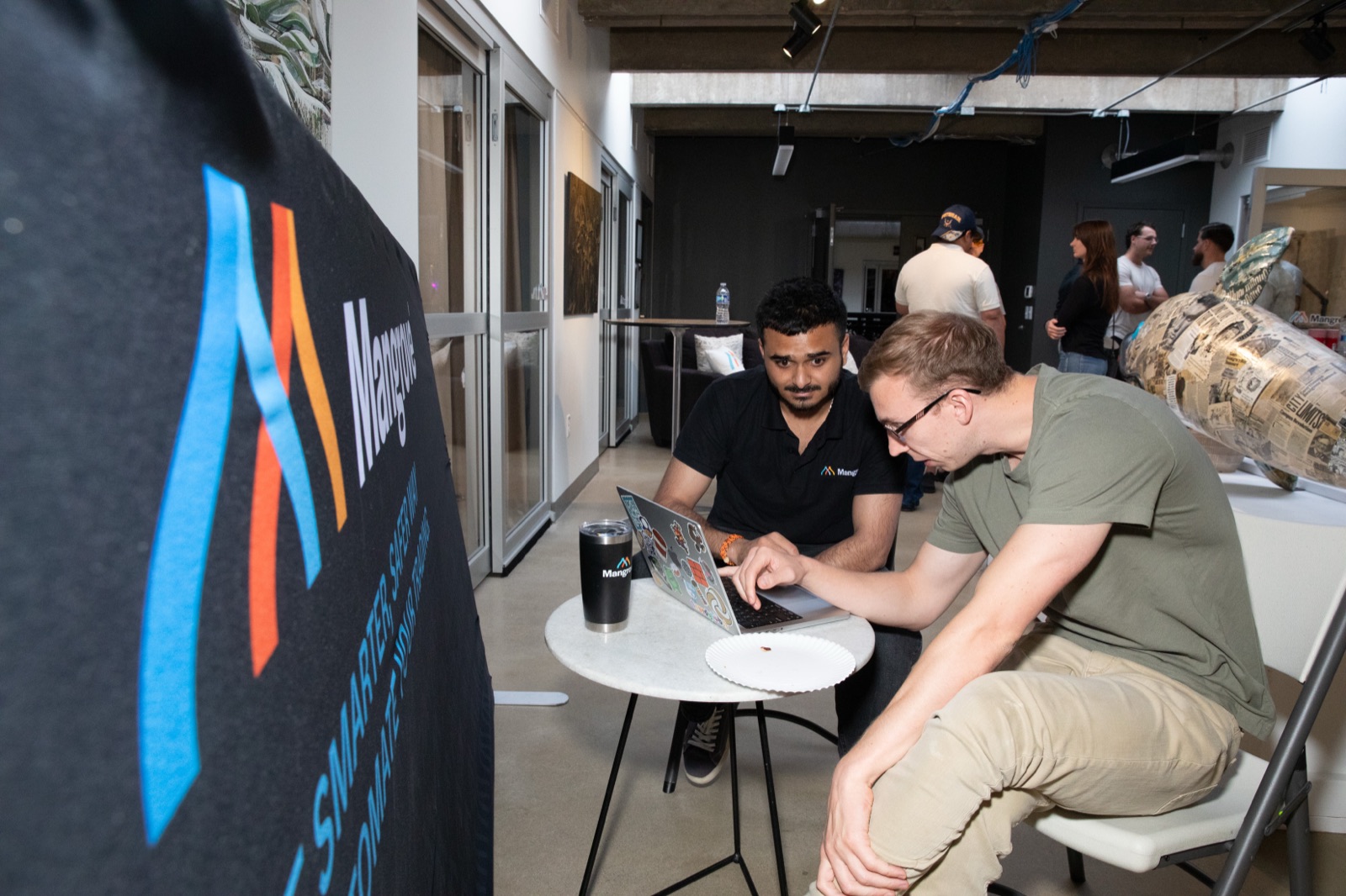 Two people working on a laptop beside a Mangrove banner